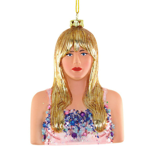 A glass Christmas ornament featuring a stylized female figure with long blonde hair and bright red lipstick, wearing a pink top with glitter accents, resembling a portrait of a pop star.