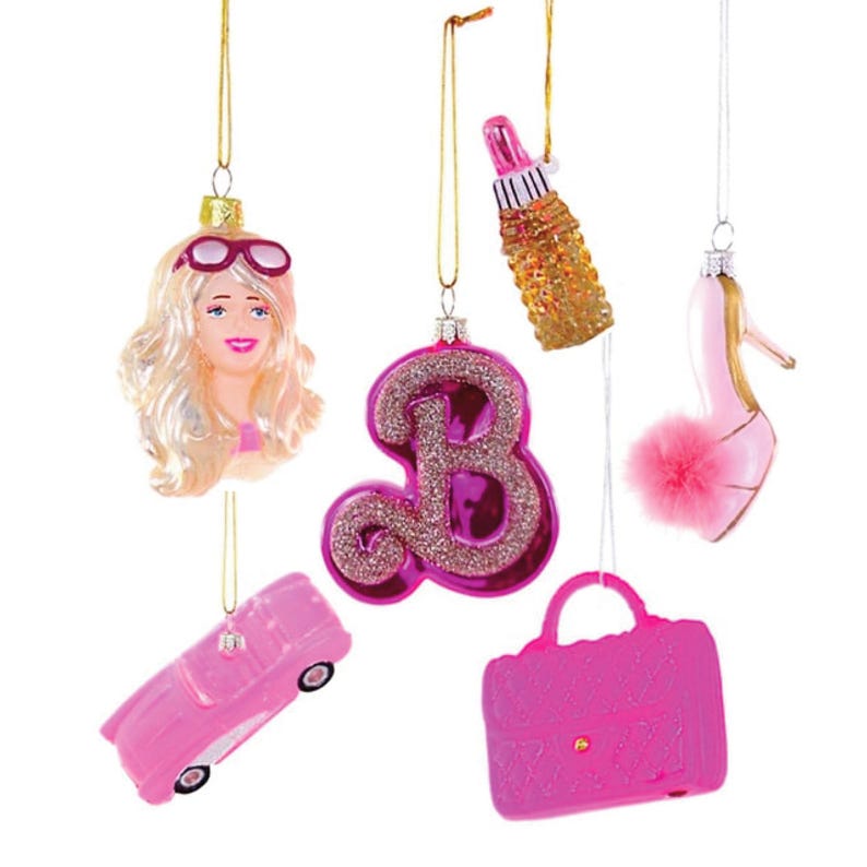Set of glass ornaments including a Barbie doll face with blonde hair and sunglasses, letter 'B', high heel shoe with fuzzy pom pom, pink lipstick in gold case, pink Corvette, and pink handbag on a white background.