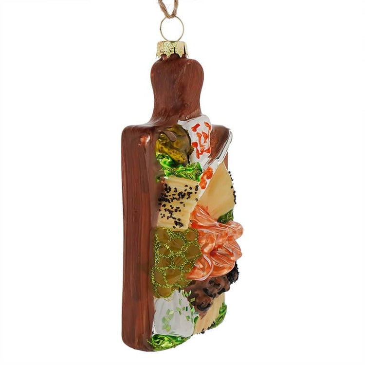 Decorative ornament featuring sliced meats, cheese, and pickles on a wooden board with a white background