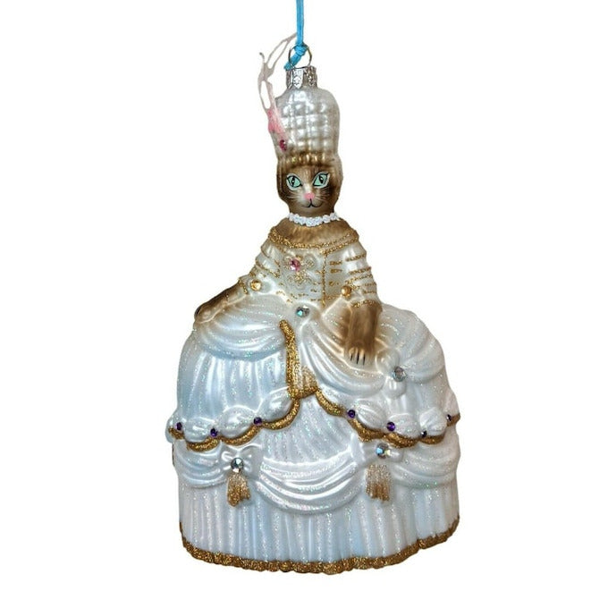 A glass Christmas ornament shaped like a regal woman but with a cat face and with cat paws in an ornate pale blue gown with gold detailing, hanging from a blue ribbon against a plain white background.
