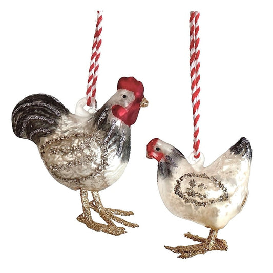 A glass rooster ornament and a glass hen ornament, both hanging from red and white striped strings on a white background.