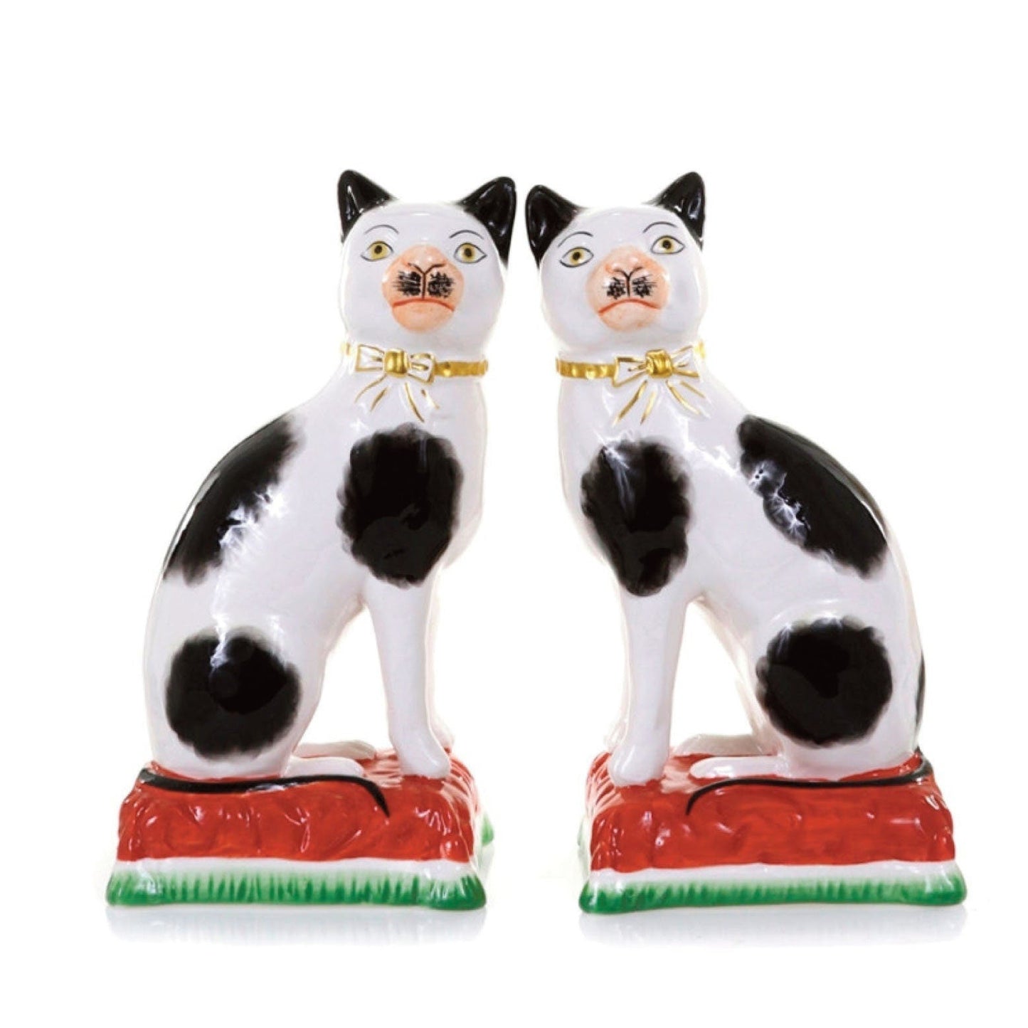 A pair of glossy ceramic cat figurines in white with black spots sitting side by side on red bases with green trim, photographed against a plain white background.