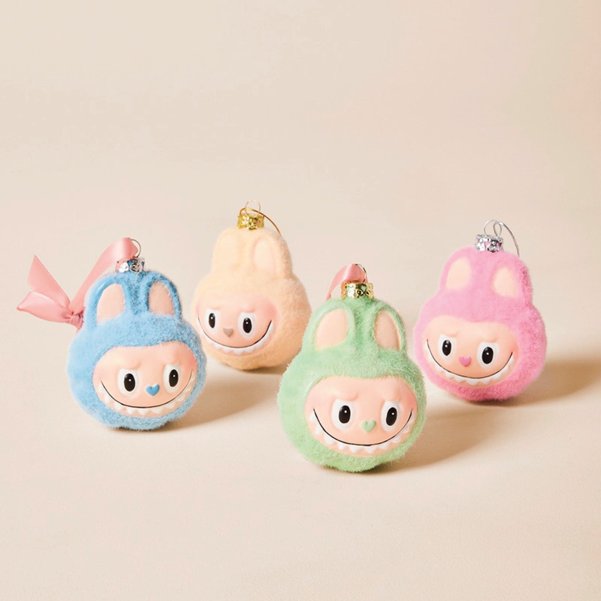 Four colorful plush ornaments shaped like sweet cartoon monster heads on a beige background